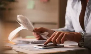 Kobieta z fakturami i telefonem komórkowym przy biurku.